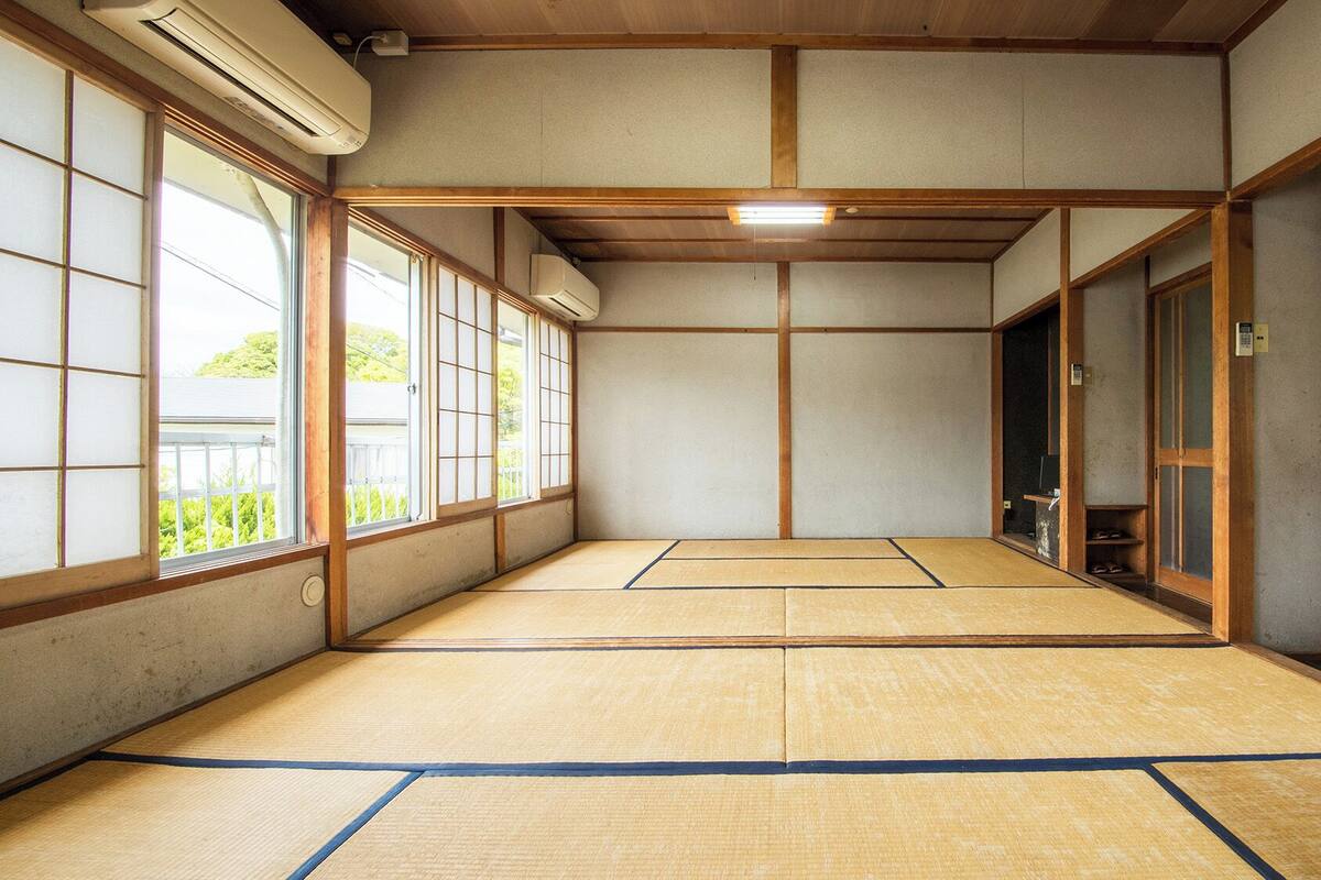 Um quarto com esteiras de tatame, portas de correr, ventoinha no teto e vista pelas janelas.