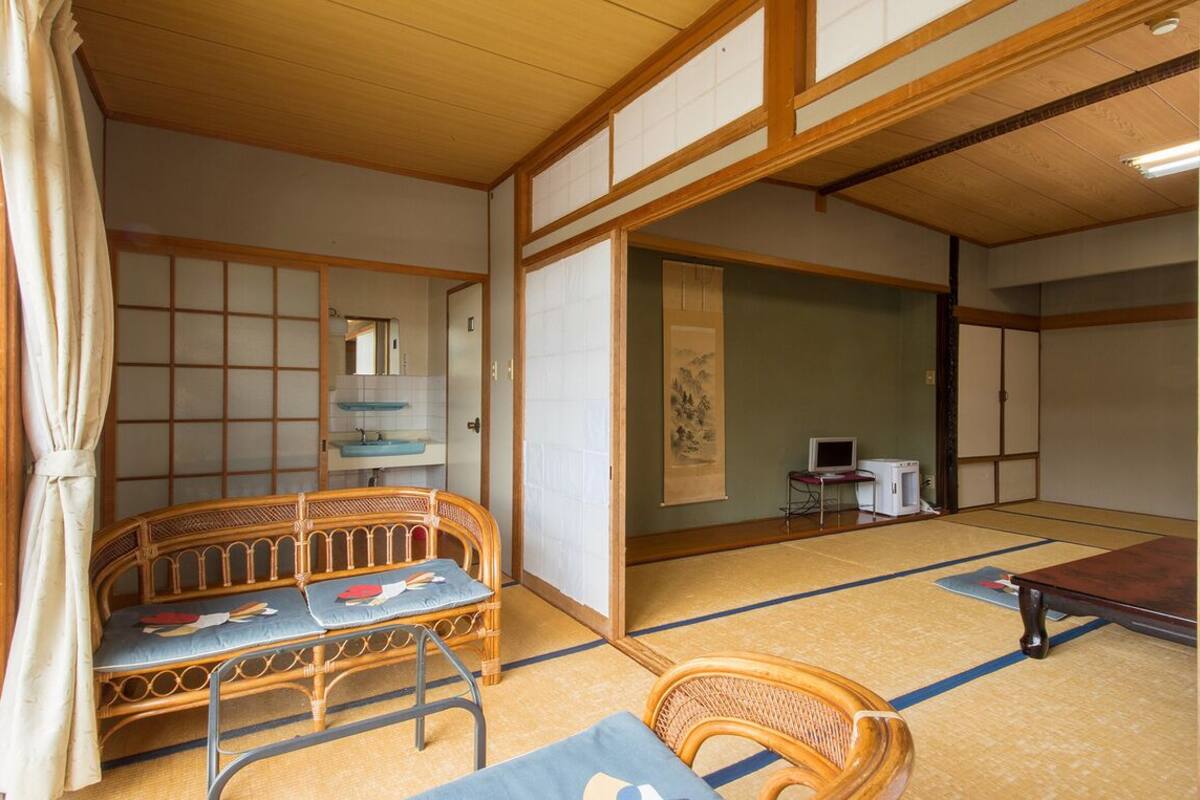 Um quarto japonês tradicional com tatames, uma mesa de madeira baixa, uma cadeira de palha e um futon.