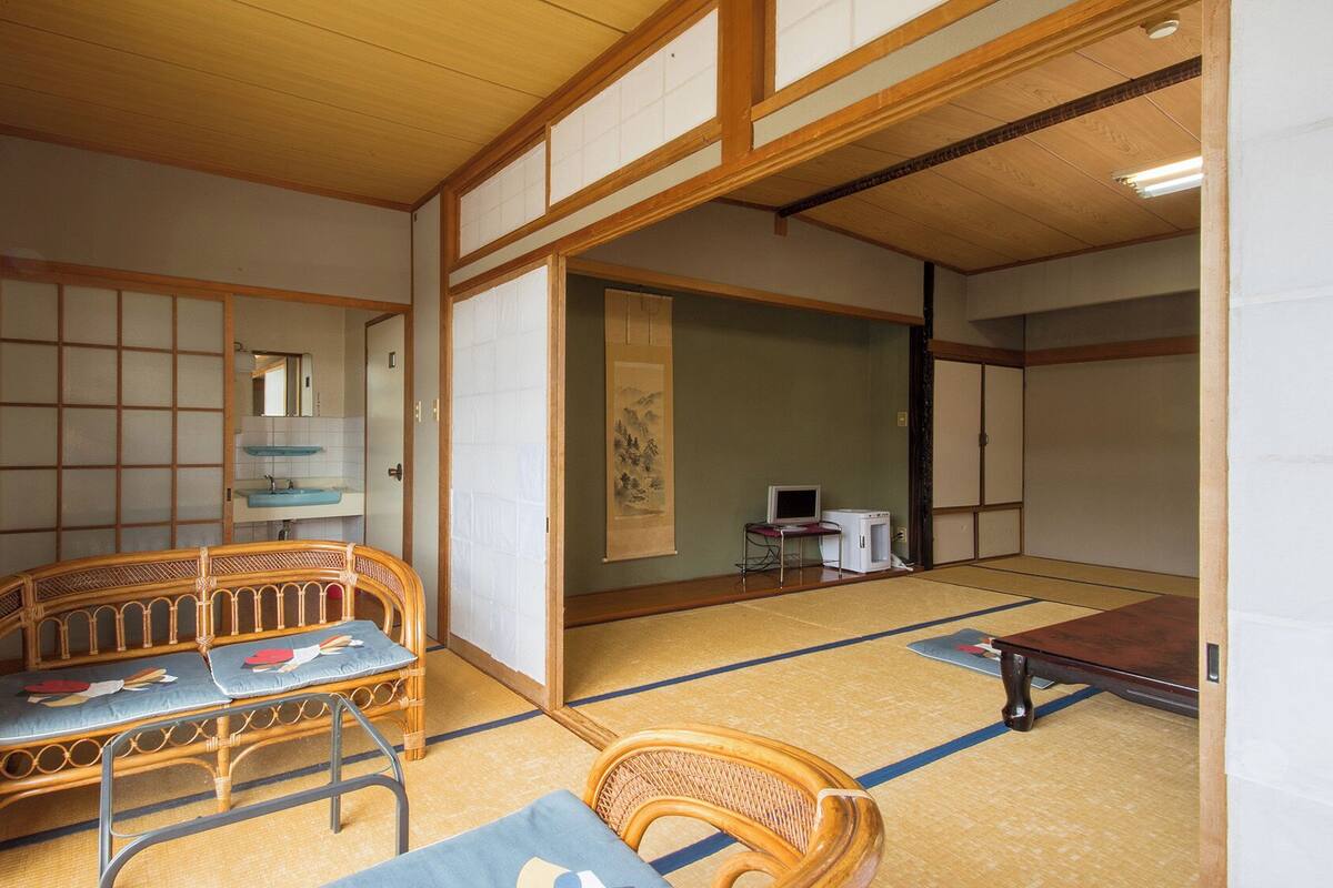 Um quarto japonês tradicional, com piso de tatame, uma mesa de madeira baixa, um sofá e uma cadeira de tatame.