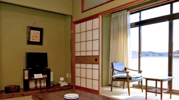 Ein traditioneller japanischer Raum mit Tatami-Bodenbelag, einem niedrigen Holztisch, einem Fernseher und Blick auf das Wasser.