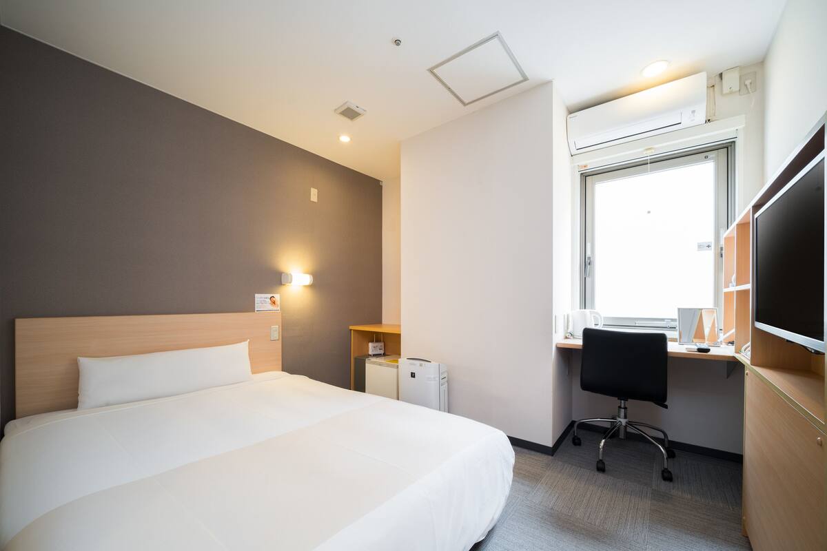 A hotel room with a large bed, a desk with a computer, and a window.