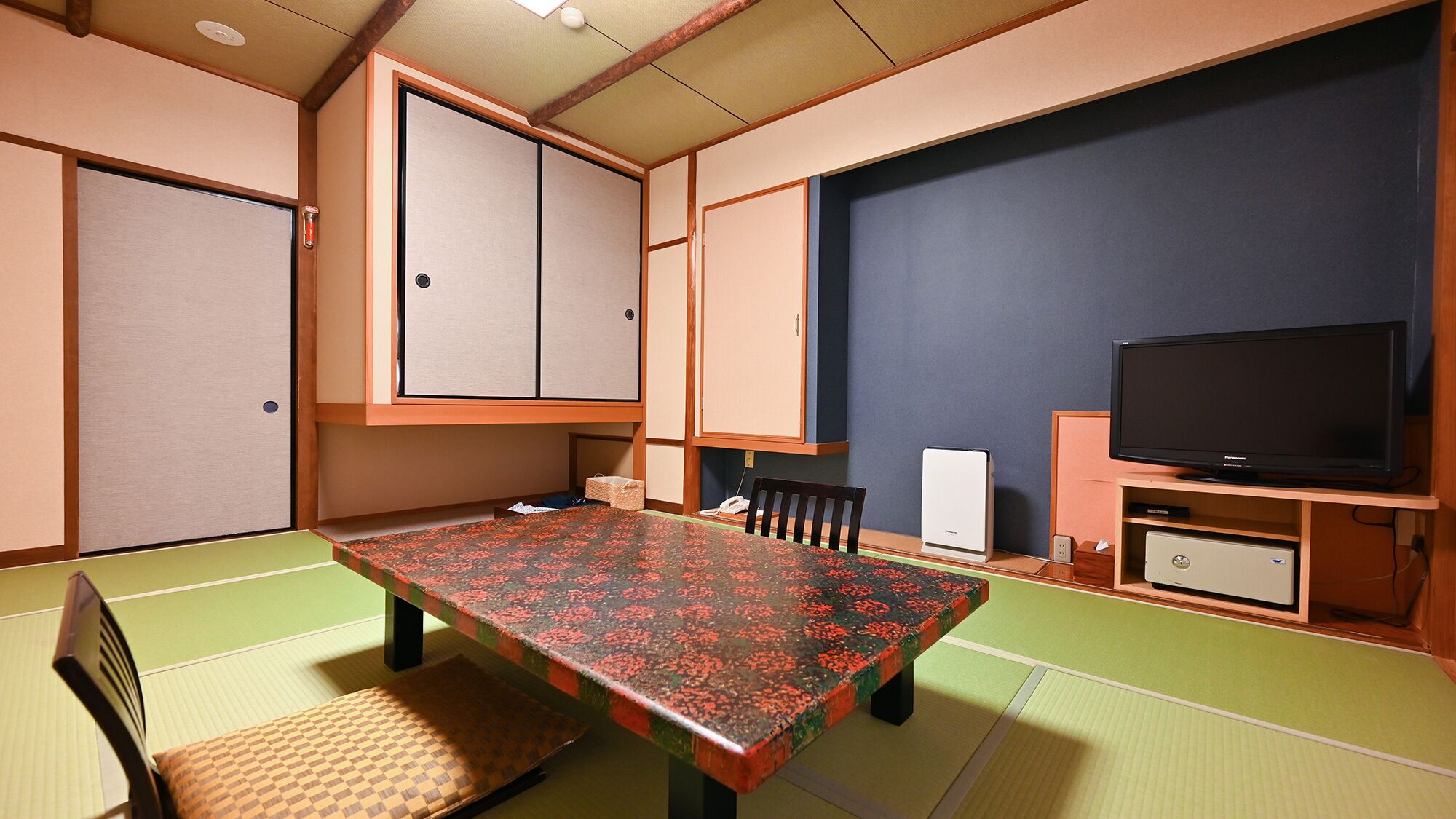 Une pièce de style japonais traditionnel, avec un sol recouvert de tatamis, une table basse, un téléviseur et un meuble.