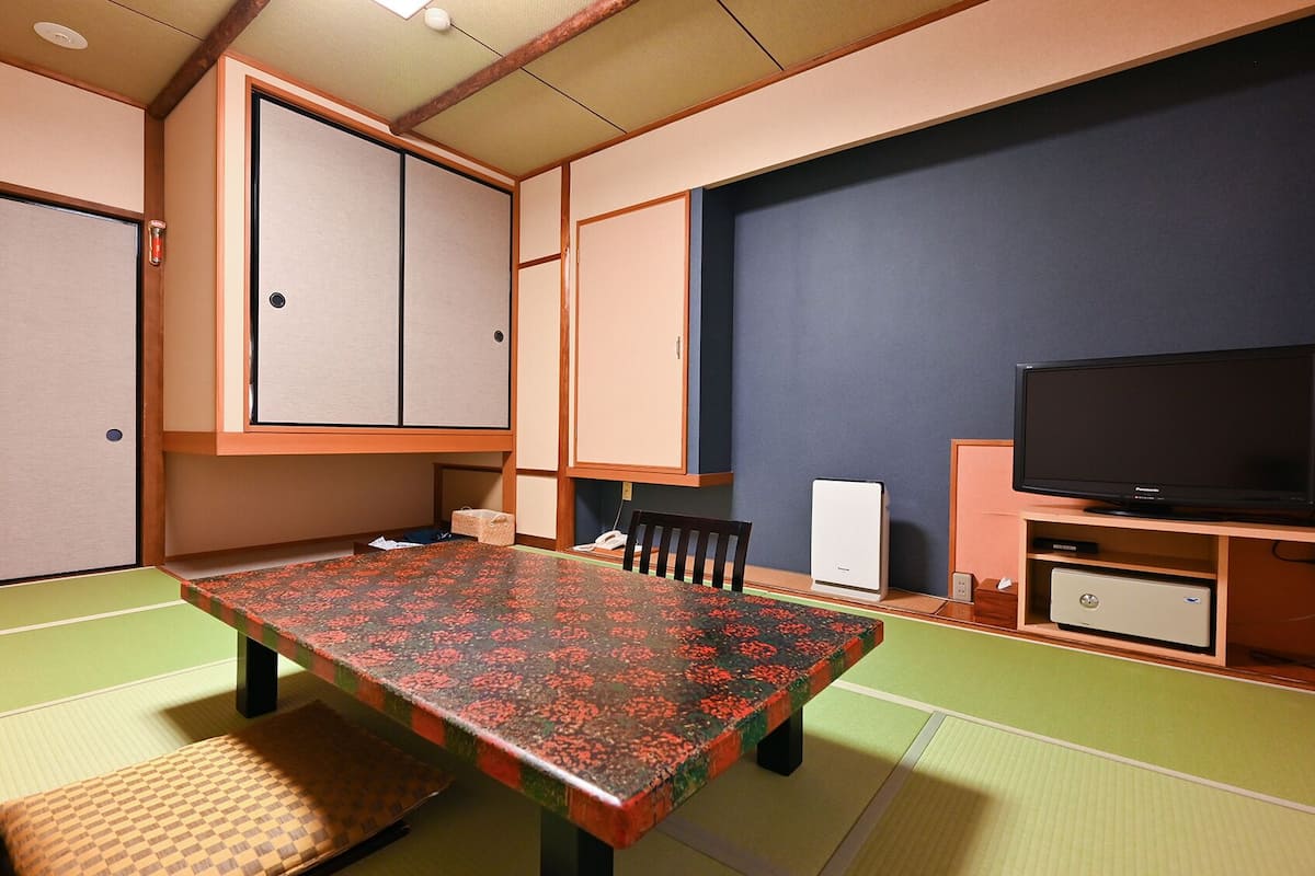Una habitación tradicional japonesa con suelo de tatami, una mesa baja, un televisor y un armario.