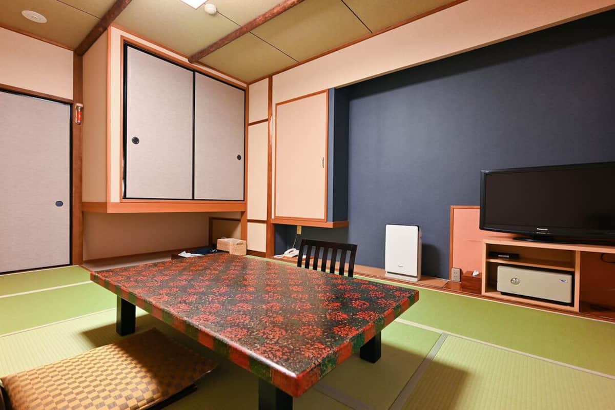 Una habitación japonesa tradicional con suelo de tatami, una mesa baja, un televisor y puertas correderas.
