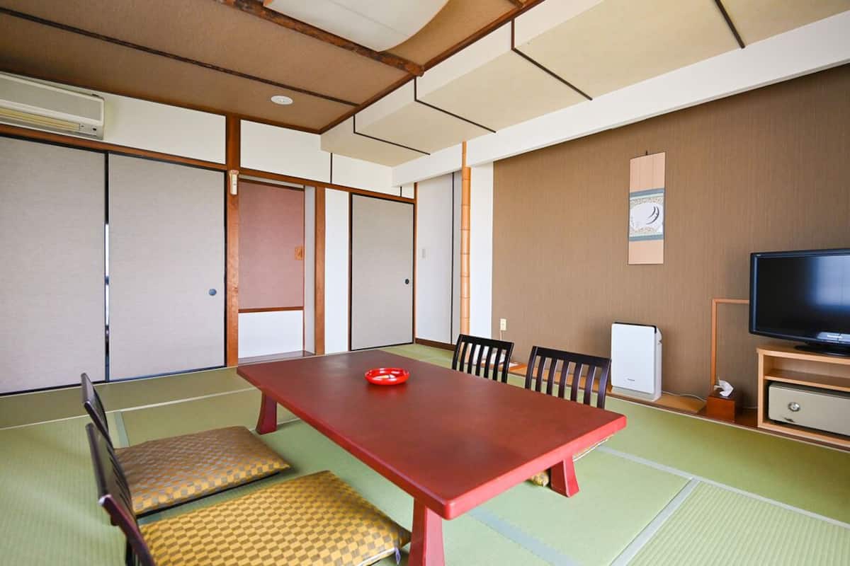 Una habitación tradicional japonesa con suelo de tatami, una mesa de madera baja y un televisor sobre un soporte de madera.