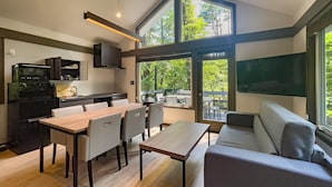 Una cocina moderna con comedor, sofá y un amplio ventanal con vistas a árboles.