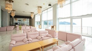 Ein großzügiger Loungebereich mit verschiedenen Sitzgelegenheiten und großen Fenstern mit Blick aufs Meer.