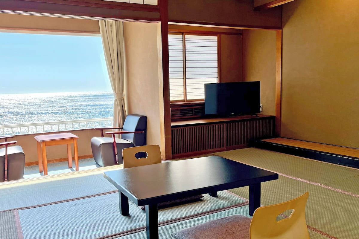Quarto com vista para o mar, televisão, mesa e duas cadeiras.