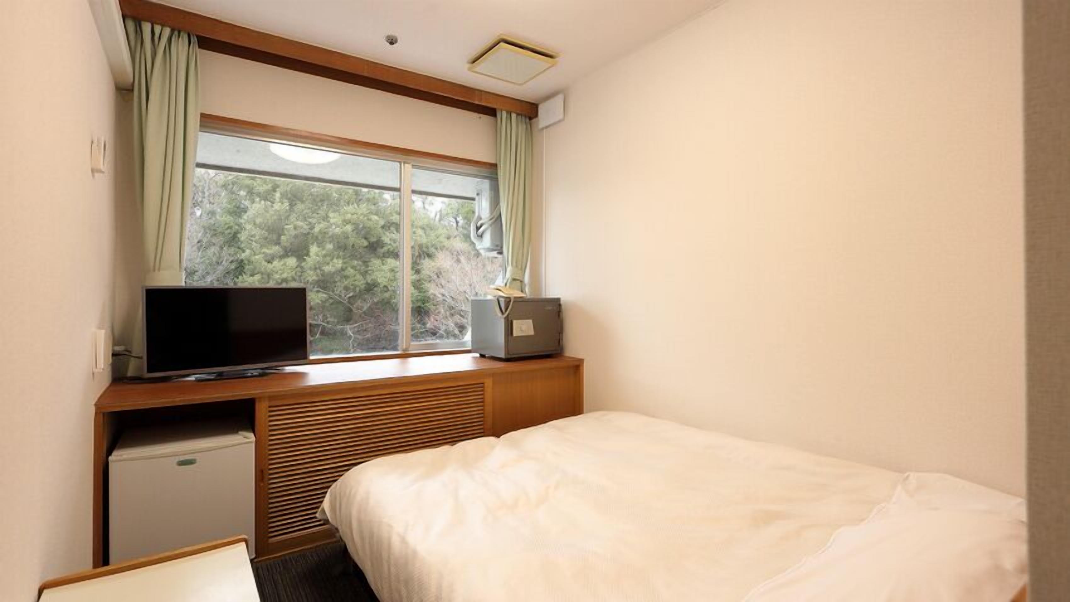 Ein Hotelzimmer mit einem Bett, einem Fernseher, einem kleinen Schreibtisch mit Computer und einem Fenster mit Vorhängen.