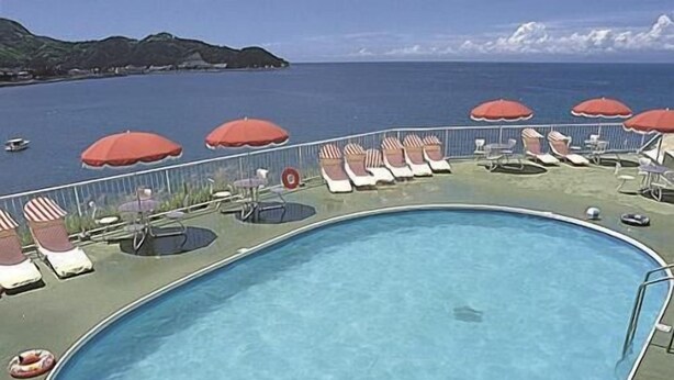 A pool with lounge chairs and umbrellas, surrounded by a railing, overlooking a body of water. - Itoen Hotel Toi (Izu)