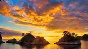 A sunset over a coastal landscape with rocky outcrops and calm water. - Itoen Hotel Toi (Izu)