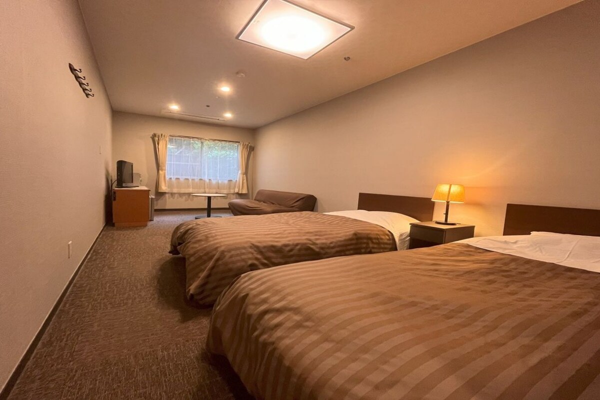 A hotel room with two beds, a desk, a chair, a lamp, and a window with curtains.