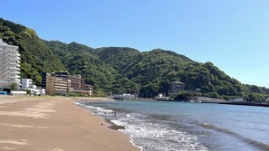 A beach with a sandy shore and a building complex in the background. - Itoen Hotel Toi (Izu)
