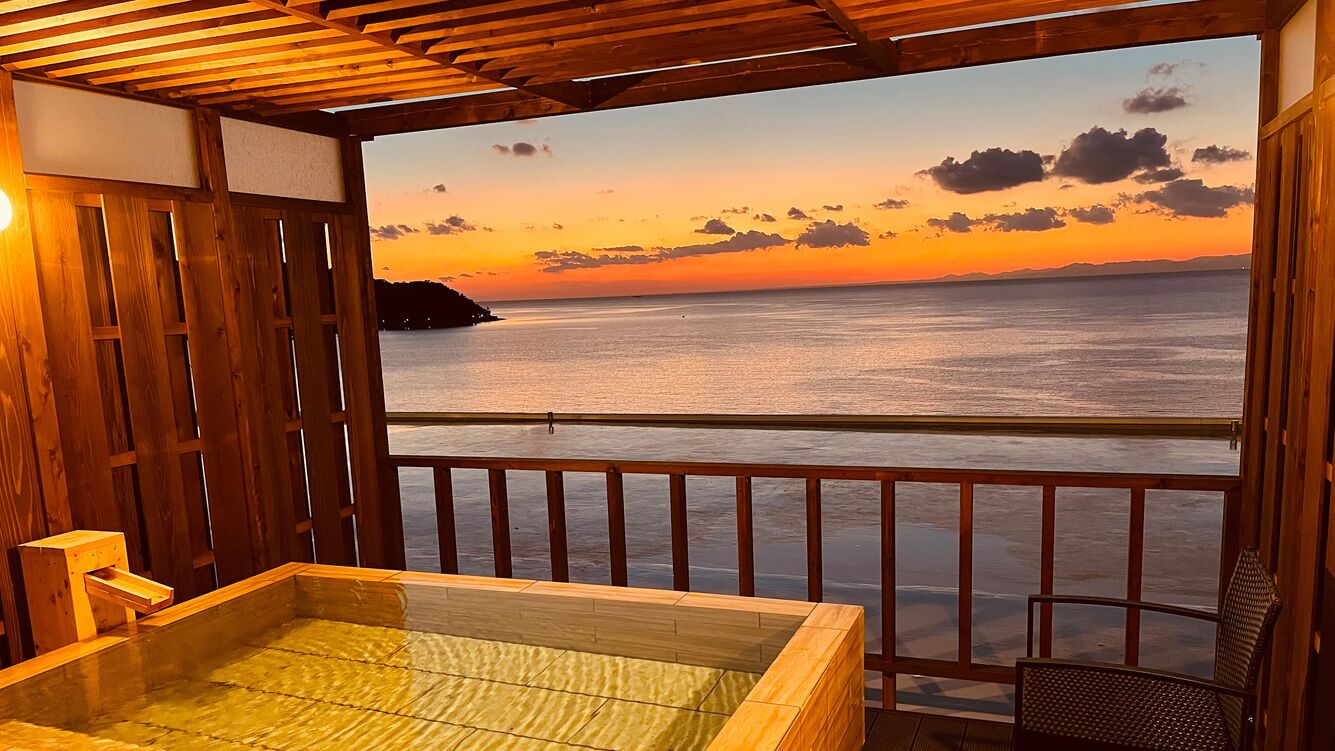Eine Holzterrasse mit Whirlpool, einem Stuhl und Blick auf das Meer bei Sonnenuntergang.