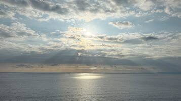 A calm sea with sunlight breaking through clouds, a distant horizon, and a small boat.
