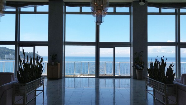 A spacious room with large windows, a chandelier, and potted plants. - Itoen Hotel Toi (Izu)
