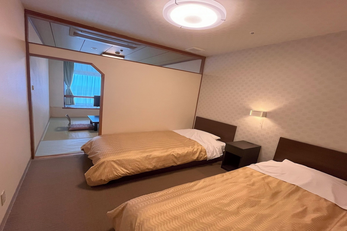 A hotel room with two beds, a small bedside table, a mirror, and a ceiling light.