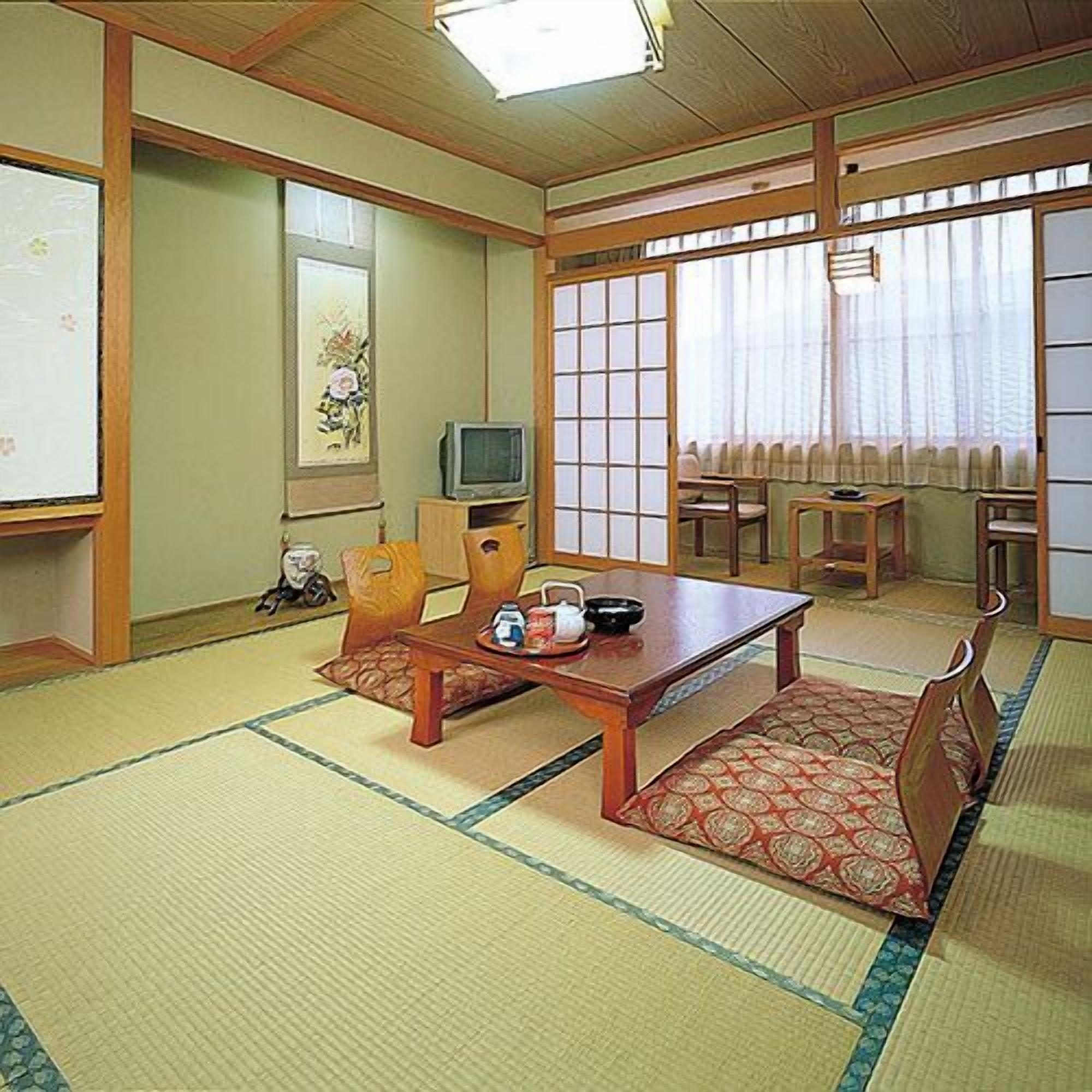 Una tradizionale stanza in stile giapponese con pavimento in tatami, un tavolino e un televisore.