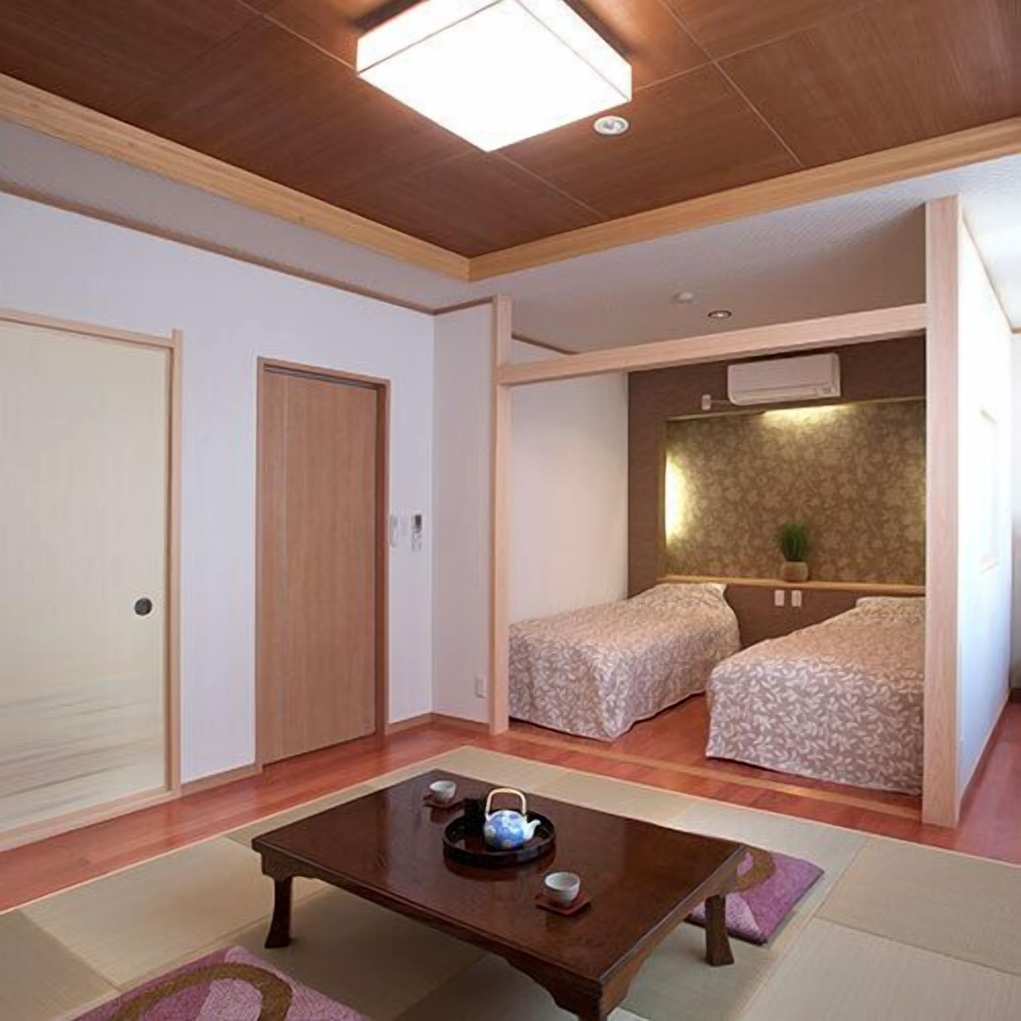 Una stanza con soffitto in legno, due letti con biancheria a motivi decorativi, un tavolo in legno con teiera e tazze, e una piccola pianta su uno scaffale.