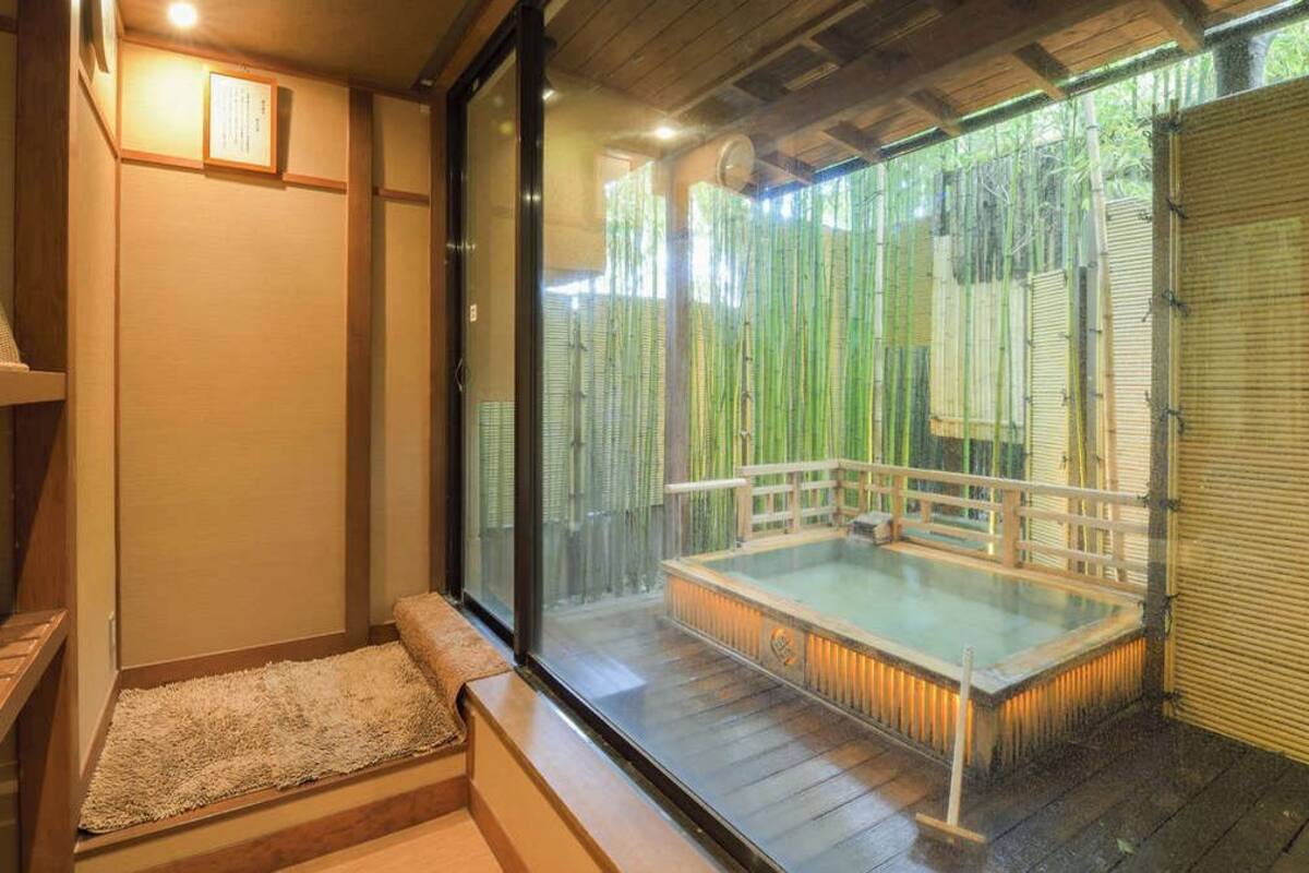 Ein traditionelles japanisches Onsen mit einer Holzdielen-Terrasse, einem in Glas eingefassten Thermalbad und Bambuswänden.