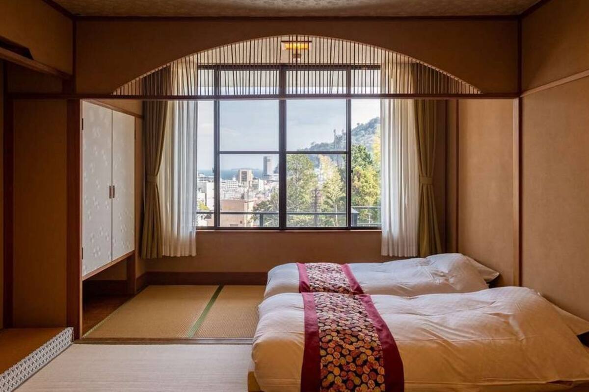 Ein Zimmer mit zwei Betten, Blick auf eine Stadtlandschaft und einer traditionellen japanischen Schiebetür.