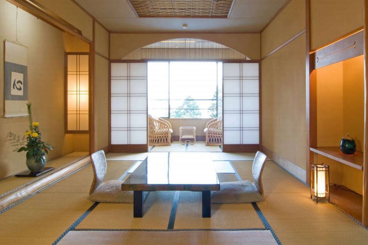 Ein traditioneller japanischer Raum mit Tatami-Böden, einem niedrigen Tisch, zwei Stühlen, einem Fenster mit Aussicht und einer Laterne.