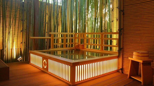 Banheira de hidromassagem com deck de madeira e paredes de bambu.