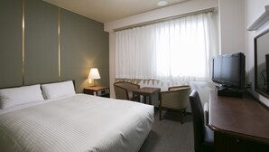 Ein Hotelzimmer mit einem Bett, einem Schreibtisch, einem Sessel, einem Fernseher und einem fenster mit Vorhängen.