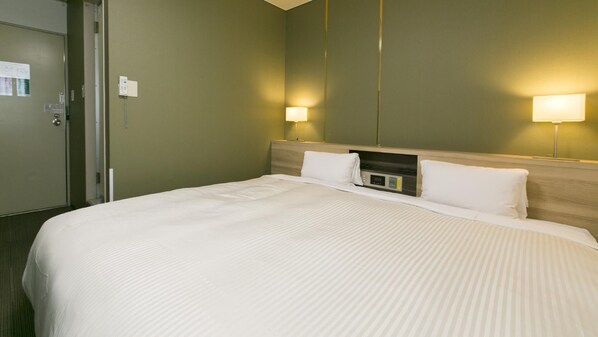 Habitación de hotel con una cama grande, dos lámparas de noche, un panel de control en la cabecera y una puerta con cerradura.