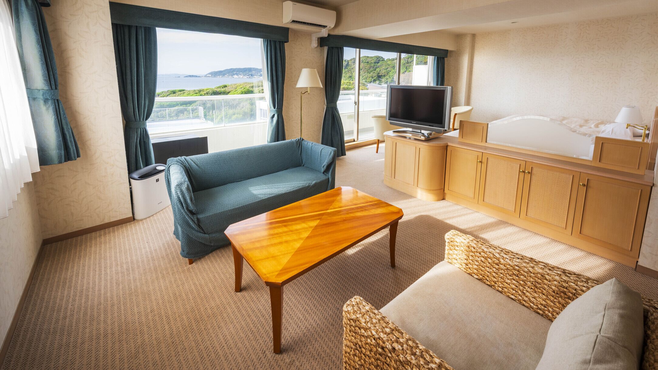 A room with a sofa, a wooden table, a TV, and a view of the sea.