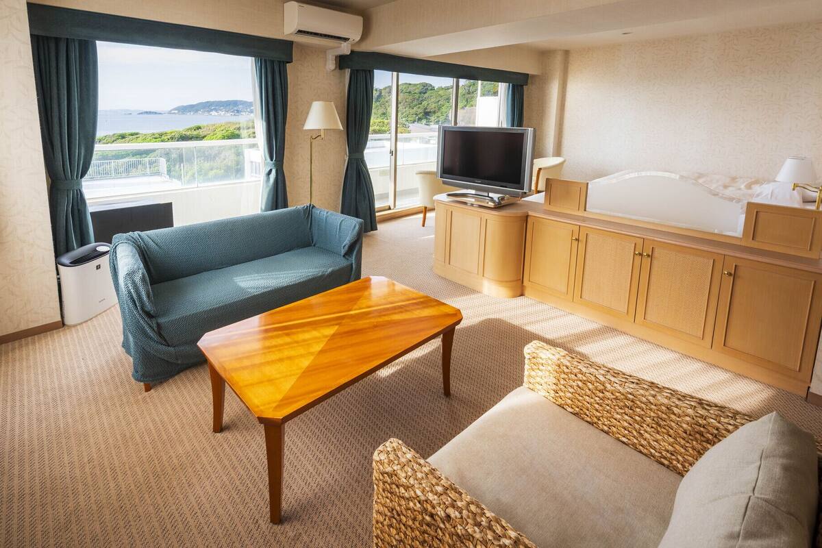 A room with a sofa, a wooden table, a TV, and a view of the sea.