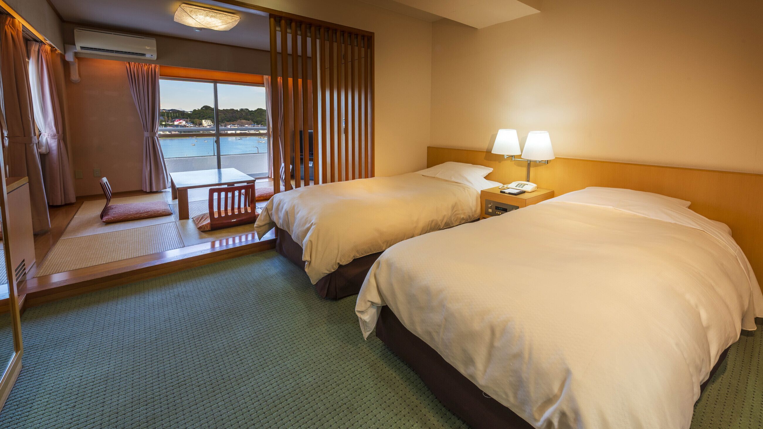Hotelkamer met twee bedden, een kleine tafel, een stoel en uitzicht op water, met gordijnen voor het raam.