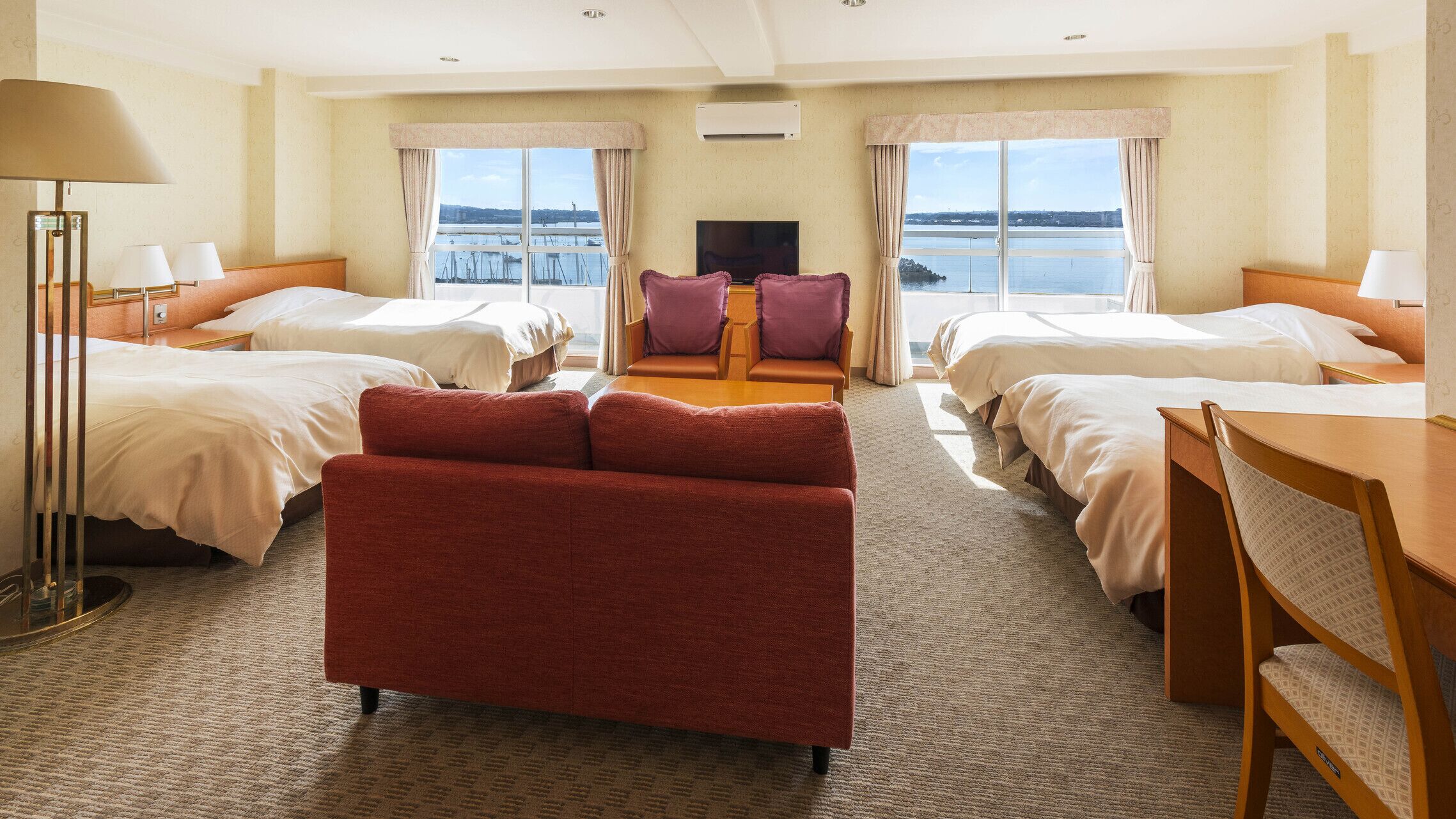 A hotel room with two beds, a sofa, a TV, and a view of the water.