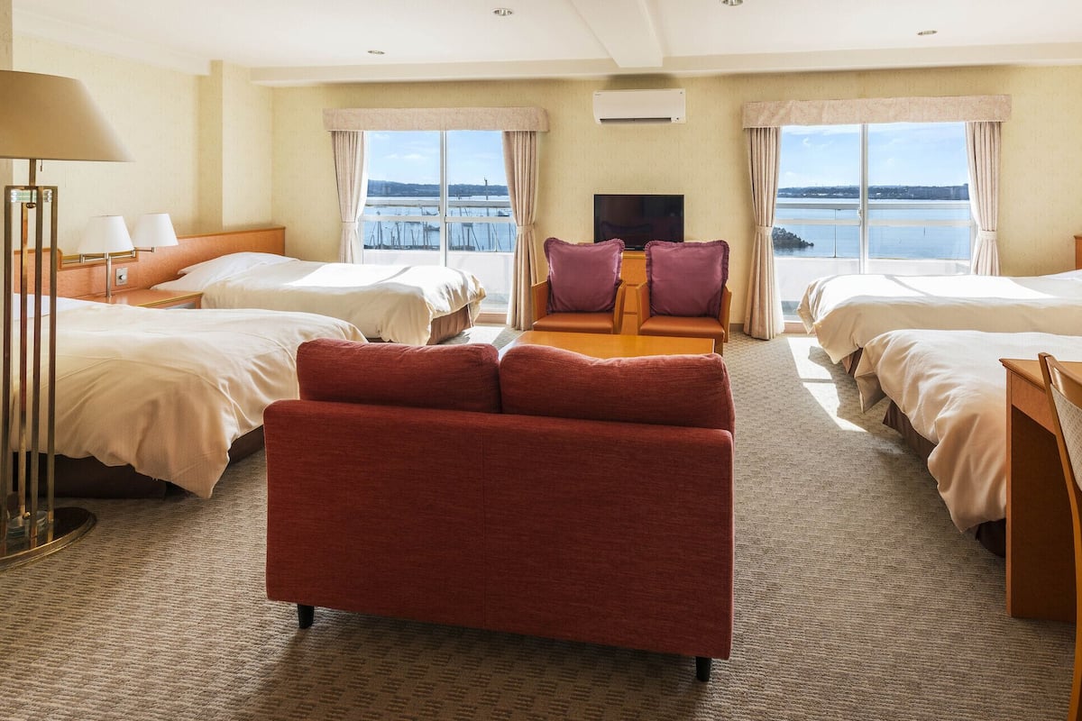 A hotel room with two beds, a sofa, a TV, and a view of the water.