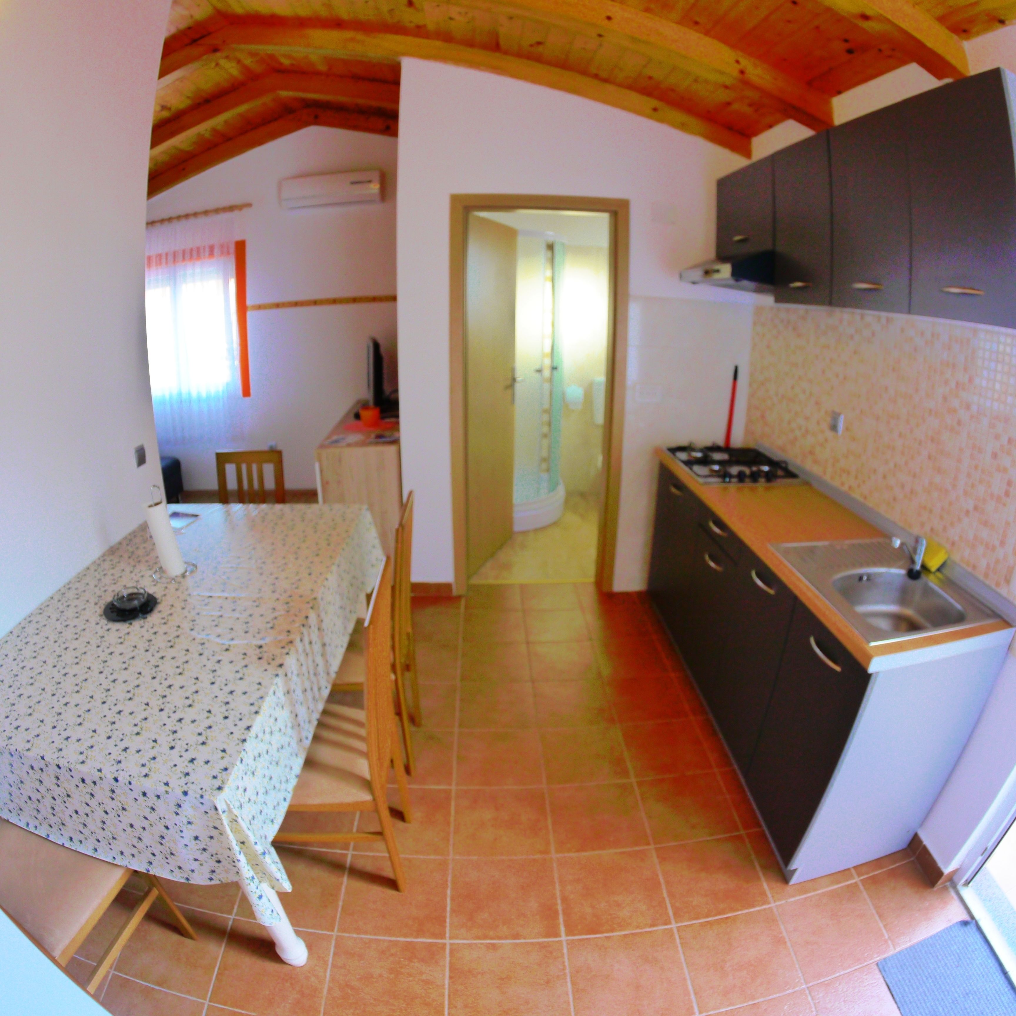 A compact kitchen with a dining area, wooden ceiling beams, and a tiled floor.