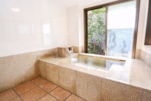 A bathroom with a bathtub, a window, and a small table. - Hatago Ogiyama (Beppu)