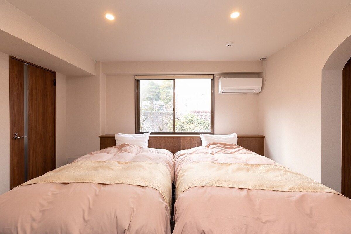 A bedroom with two beds, a window, an air conditioning unit, and a wooden door.