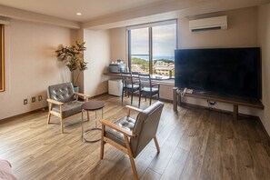 A modern living room with a large TV, two leather chairs, a small table, and a view of the city through large windows. - Hatago Ogiyama (Beppu)