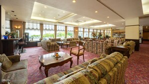 A spacious lobby with multiple seating areas, a reception desk, and large windows offering a view of the outdoors. - Noji Onsen Hotel (Fukushima)