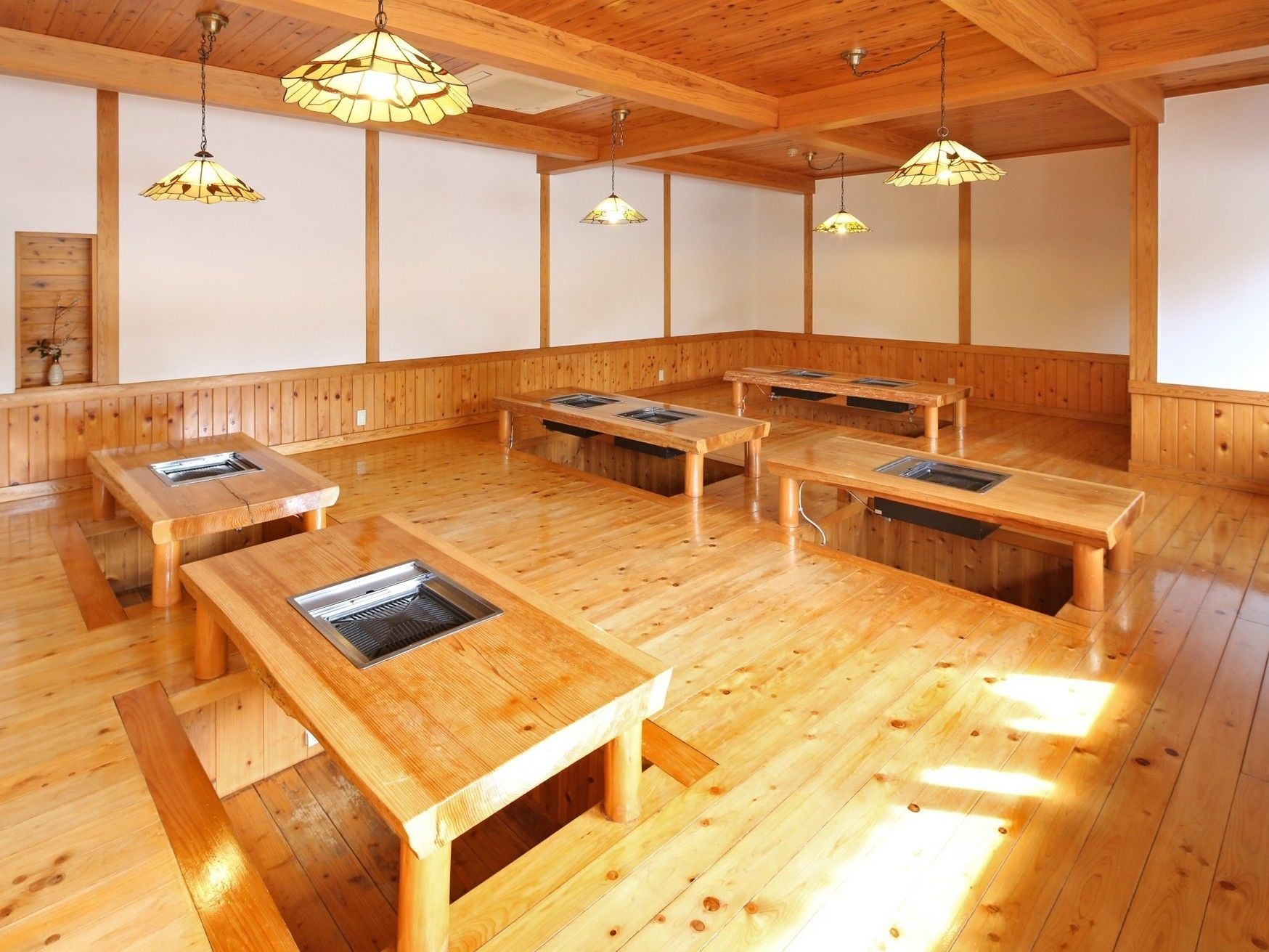 Um quarto amplo com piso de madeira e mesas, cada uma com uma churrasqueira embutida.