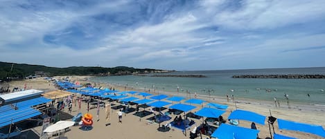 A beach with blue umbrellas and people.