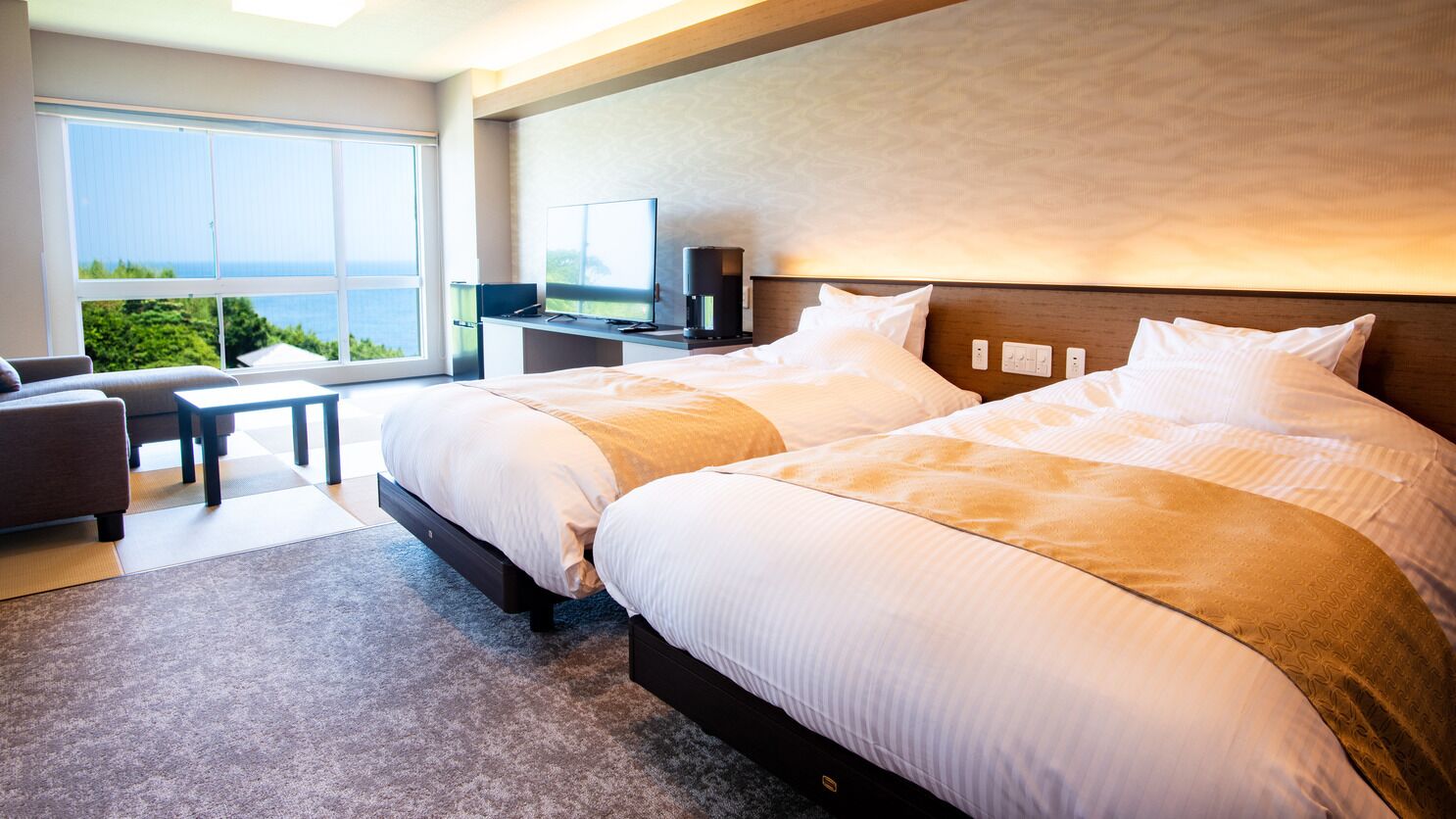 Ein Hotelzimmer mit zwei Betten, einem Schreibtisch mit Fernseher und Meerblick.