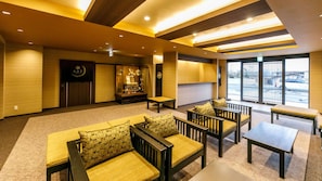 A hotel lobby with seating arrangements, a reception desk, and a view of the outside.