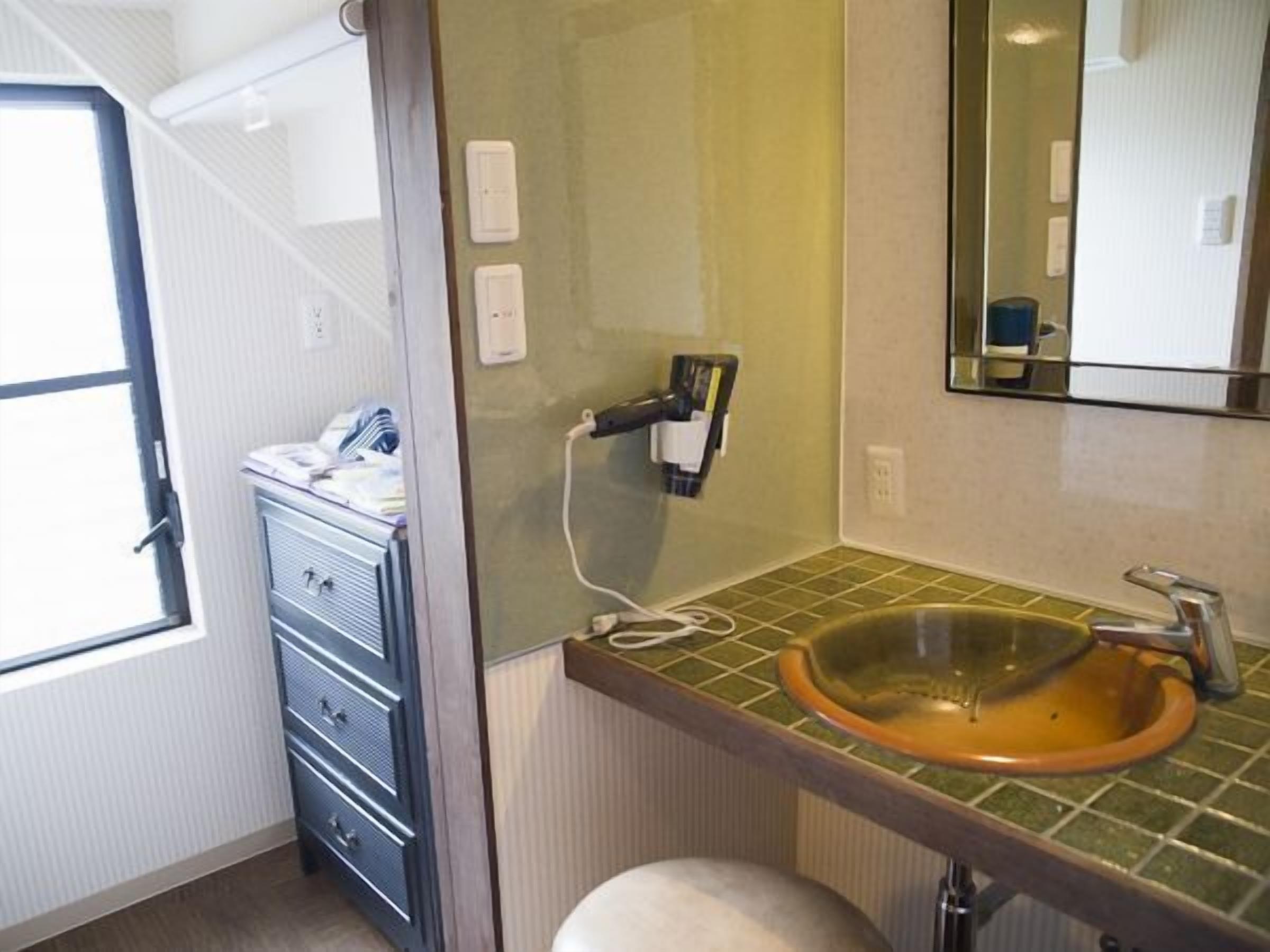 Een badkamer met een groen betegeld wastafelmeubel, een spiegel, een handdoekhouder en een raam.