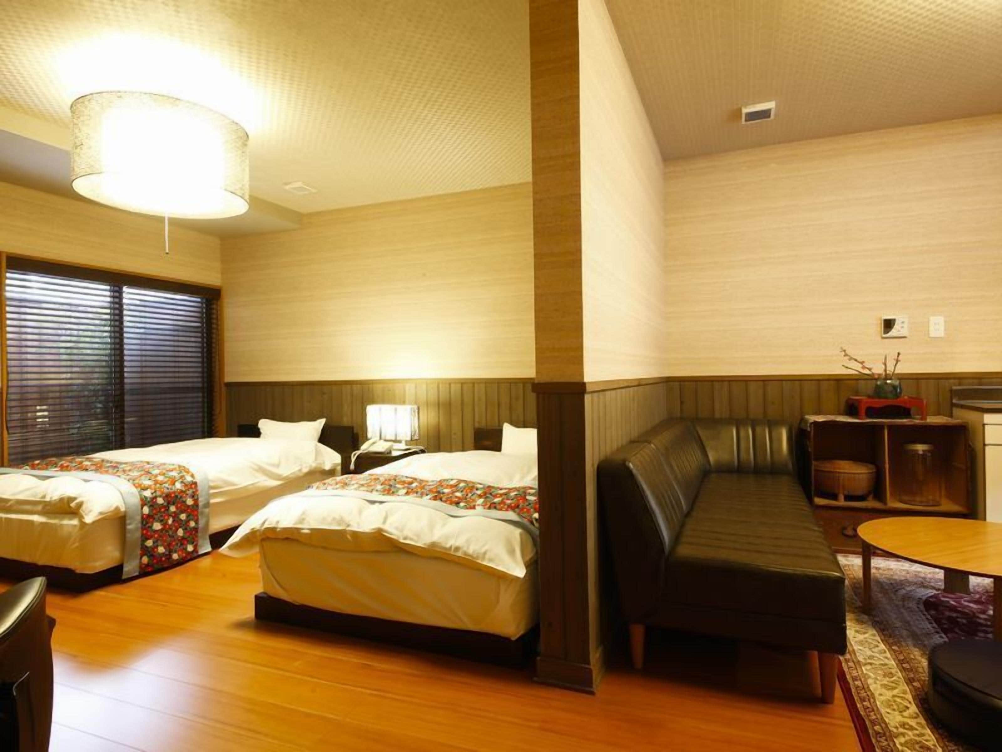 A hotel room with two beds, a sofa, a small table, and a window with blinds.