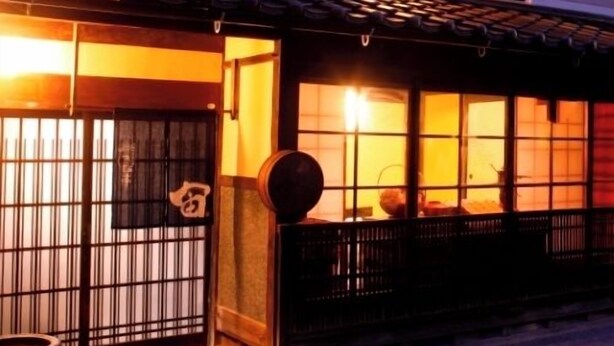 Un edificio japonés tradicional con tejado de tejas, puerta de madera con diseño de cuadrícula y un pequeño porche con banca de madera.