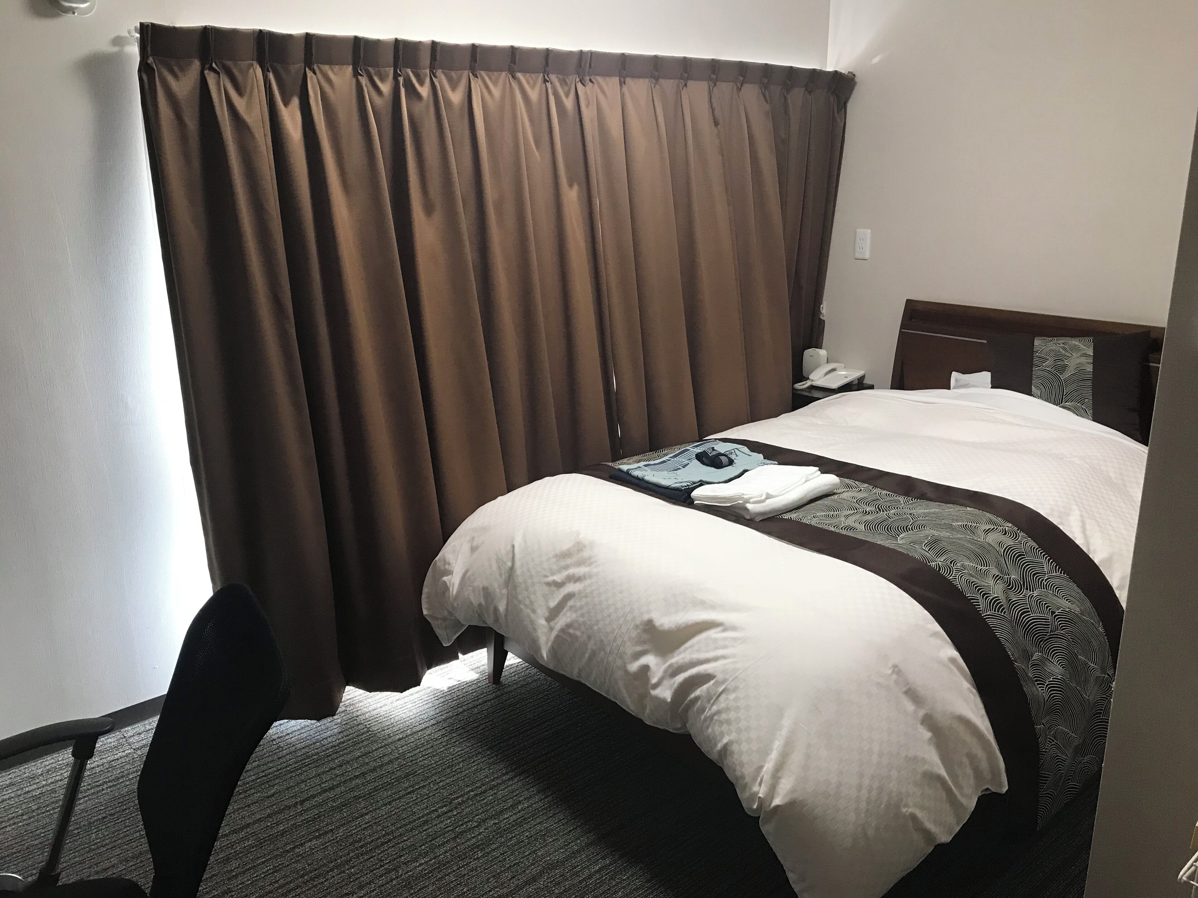 A hotel room with a bed, a chair, a desk, and a telephone.