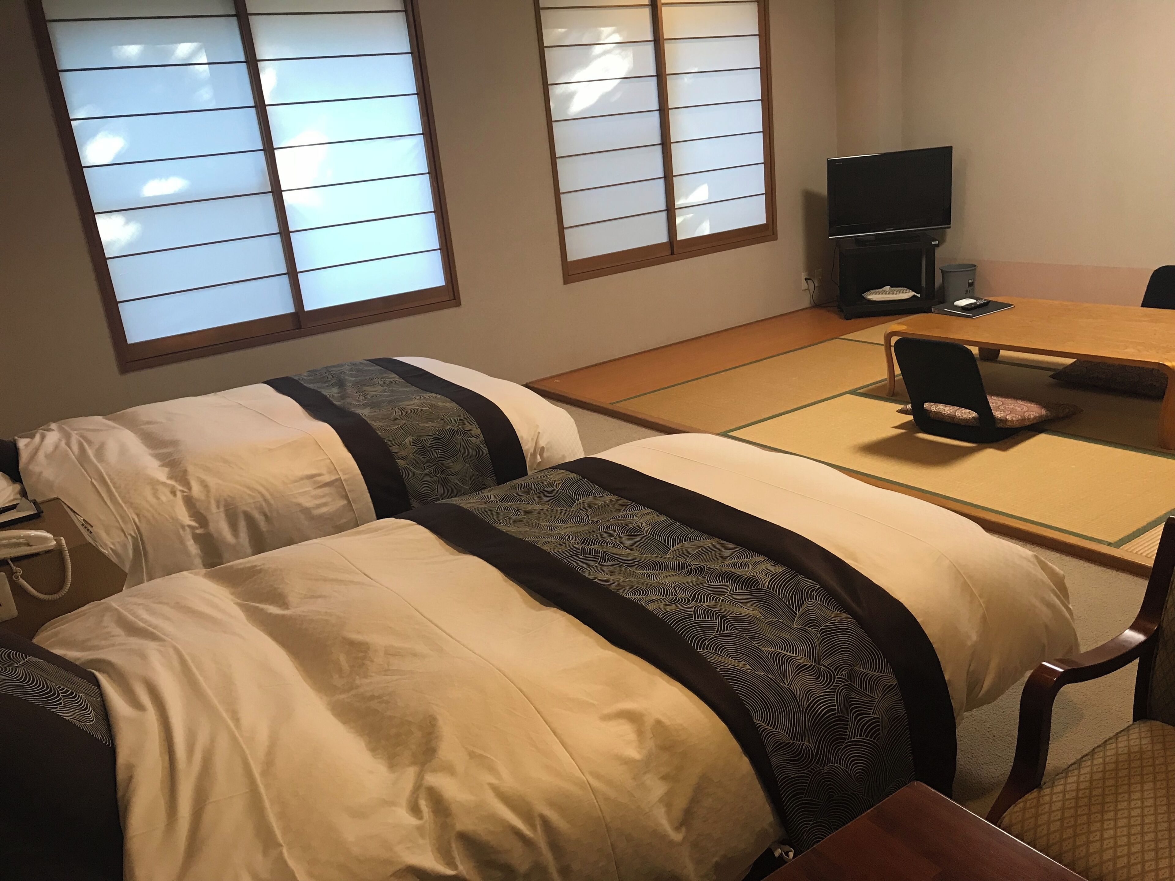 A hotel room with two beds, a dining table, a TV, and a futon.