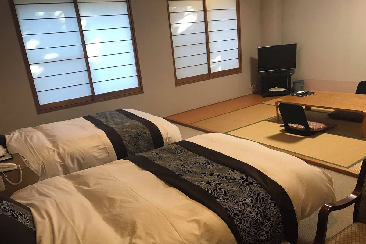 Ein Hotelzimmer mit zwei Betten, einem Esstisch, einem Fernseher und einer Schlafcouch.