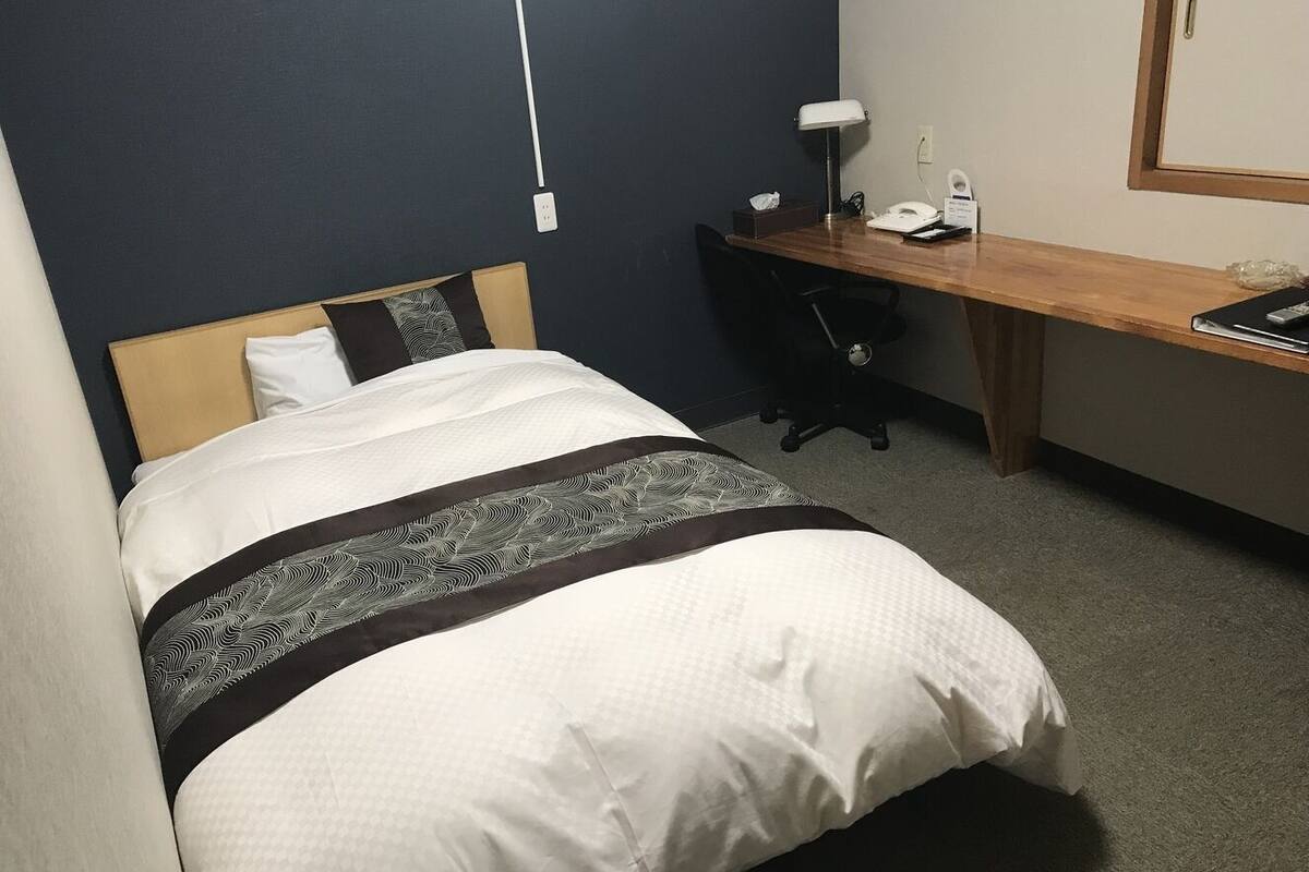 Ein Hotelzimmer mit Bett, Schreibtisch, Stuhl, Lampe und Telefon.